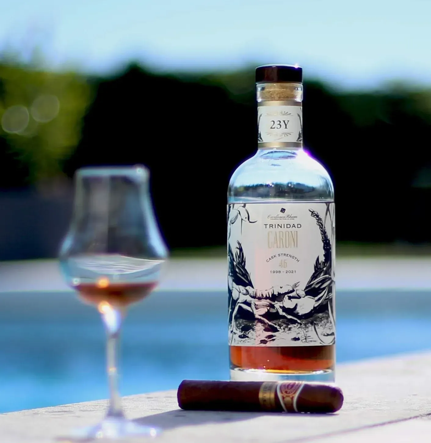 A glass of Caroni rum next to a cigar, on a dark background